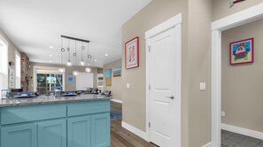 A modern kitchen with a central island, pendant lighting, and a view to the dining area. - Mac's Surf Shack at Seaside Beach (Seaside)