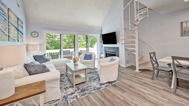 A spacious living room with a white couch, a coffee table, a fireplace, a TV, and a spiral staircase. - Sea Colony Coastal Escape: Steps from Trolley stop, pools, tennis, fitness center and more!  Private Beach! (Bethany Beach)