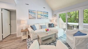 A spacious living room with a white sofa, a coffee table, and a view of the outdoors. - Sea Colony Coastal Escape: Steps from Trolley stop, pools, tennis, fitness center and more!  Private Beach! (Bethany Beach)