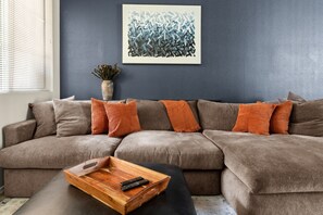 A living room with a sectional sofa, a wooden coffee table, a remote control, and a framed abstract painting on the wall. - Luxury Cave Creek Townhome Near Golf, TPC & Scottsdale (Phoenix)