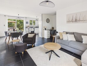 Ein modernes Wohnzimmer mit grauem Sofa, einem runden Couchtisch und einem Essbereich mit Stühlen und Tisch.
