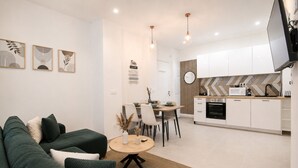 A modern living room with a green sofa, a dining area with chairs, a kitchen with white cabinets, and a TV mounted on the wall. - Calm Elegant Apartment in the Heart of Nice (Nice)