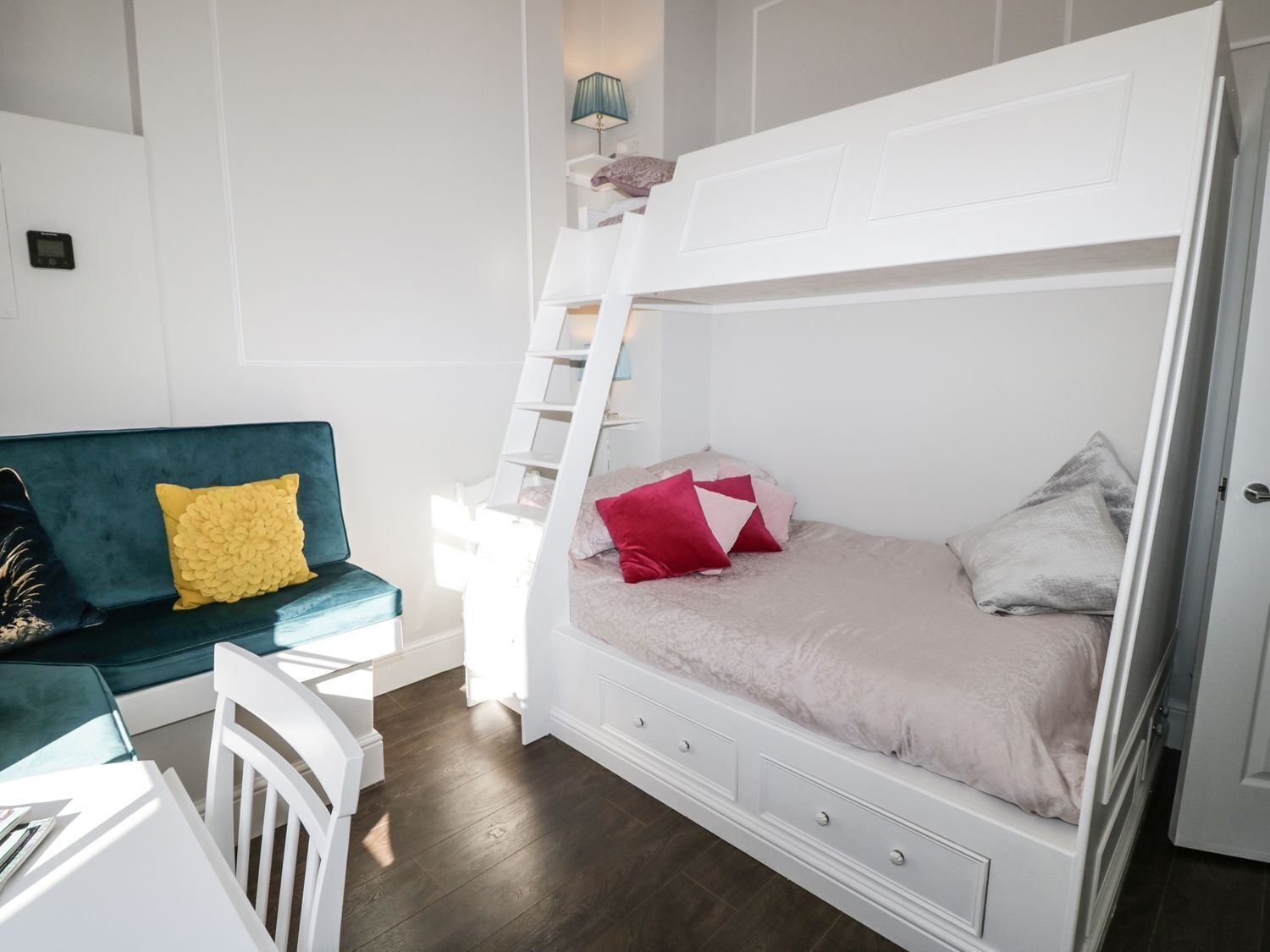 A room with a bunk bed, a white dresser, a teal sofa, and a small table.