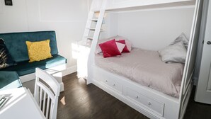 A room with a bunk bed, a white dresser, a teal sofa, and a small table. - Hamilton's Studio (Ryde)