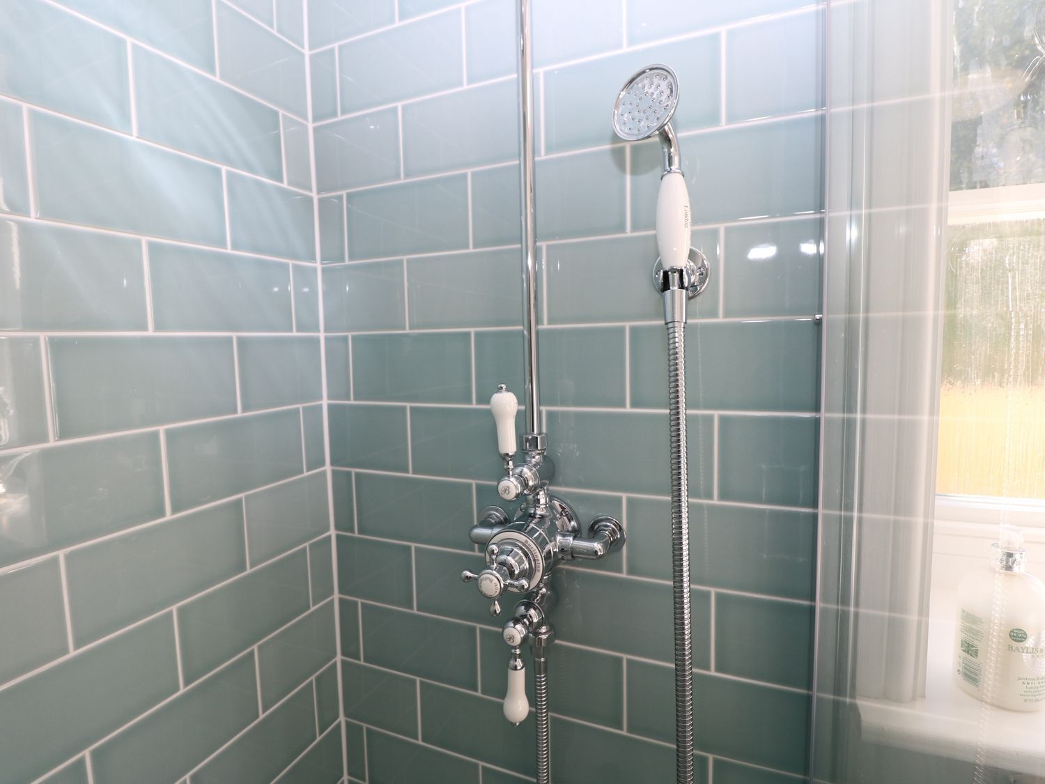 Eine Dusche mit Handbrause und wandmontiertem Wasserhahn, mit hellblauen Fliesen.