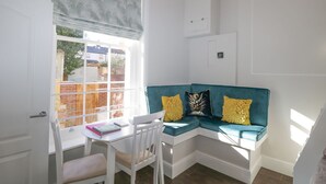 A corner room with a window, a white table with a chair, and a teal sofa with yellow cushions. - Hamilton's Studio (Ryde)