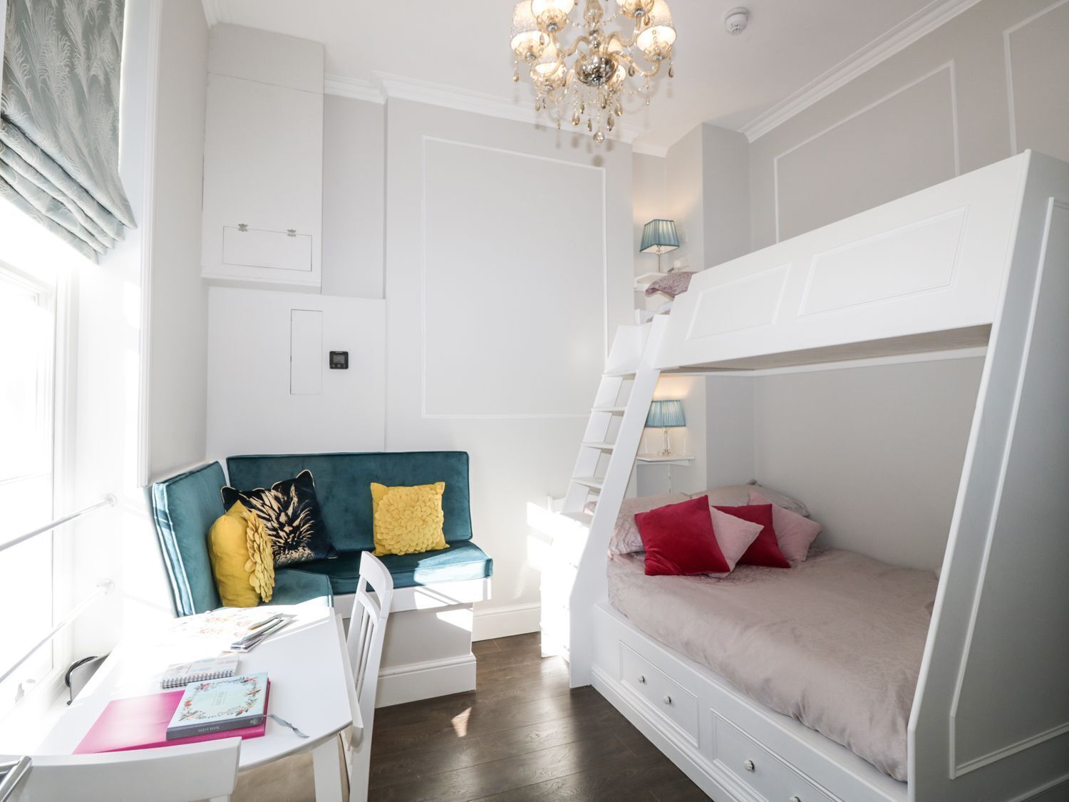 Een slaapkamer met een stapelbed, een bureau met een stoel, een bank en een kroonluchter.