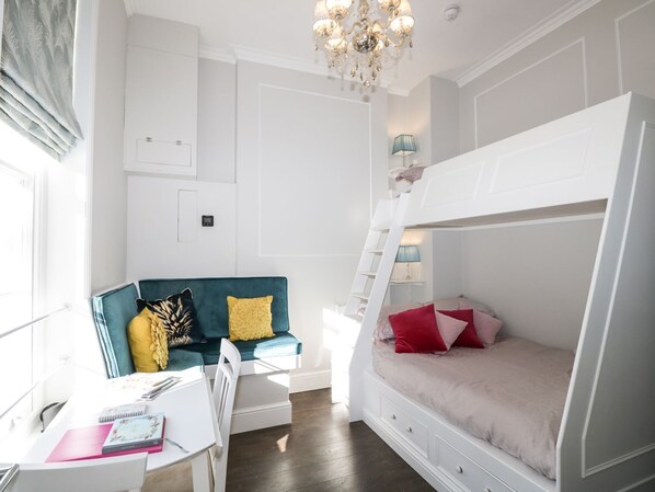 A bedroom with a bunk bed, a desk with a chair, a sofa, and a chandelier. - Hamilton's Studio (Ryde)
