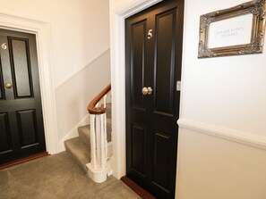 Ein Flur mit zwei schwarzen Türen, wovon eine mit der Nummer 5 gekennzeichnet ist, und einer Treppe mit weißen Geländern.