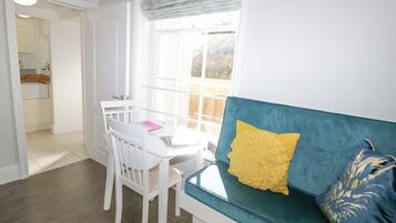 Una habitación con una mesa de comedor, sillas, un sofá azul con almohadas amarillas y una ventana con vistas al exterior.