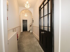 A hallway with a carpeted floor, a black door with glass panels, a white door at the end, and a chandelier. - Hamilton's Studio (Ryde)