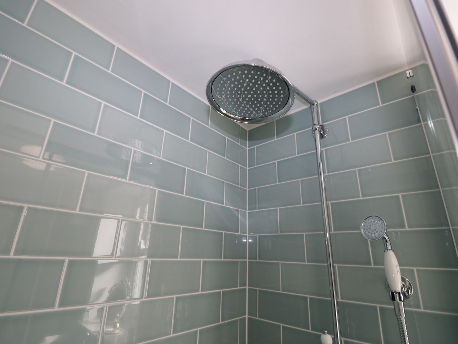 A corner shower with a handheld showerhead and a wall-mounted faucet.
