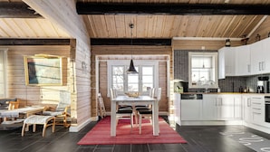 A wooden interior with a dining area, kitchen, and a red rug.