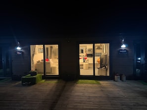 A modern building with large glass doors leading to a living area with a sofa and a kitchen visible inside. - Haggis Lodge at Three Lochs Holiday Park (Newton Stewart)