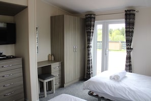 A bedroom with a bed, a desk, a chair, a television, and a wardrobe. - Haggis Lodge at Three Lochs Holiday Park (Newton Stewart)