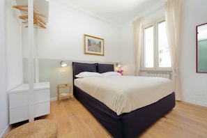 Ein Schlafzimmer mit einem Bett, Nachttischen, einem Heizkörper und einem Fenster mit Vorhängen.