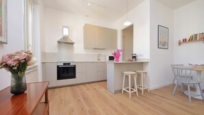 A modern kitchen with white cabinets, a microwave, and a sink. There is a wooden dining table with two stools and a small island with a stool. - Piazza Vittorio - Recently redecorated apartment for 4 (Roma)