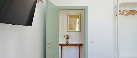 A room with a bed, a TV, a wall-mounted air conditioner, a door leading to another room, and a small table with a vase of flowers.