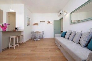 Ein modernes Wohnzimmer mit einer Couch, einem Esstisch mit Stühlen, einer Küchenzeile mit Barhocker und einem großen Spiegel.