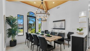 Uma zona de refeições moderna com mesa de madeira, cadeiras pretas, um candelabro e vista para o exterior.