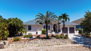 A residential house with a stone driveway, palm trees, and a clear blue sky. - Island Time on Ivory I 4 Bed Waterfront Home (Marco Island)