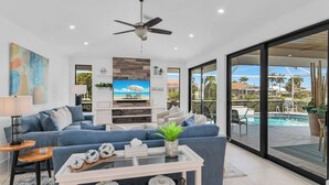Uma sala de estar moderna com sofá, mesa de centro, TV e vista para uma piscina.