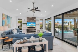 A modern living room with a sofa, coffee table, TV, and a view of a swimming pool. - Island Time on Ivory I 4 Bed Waterfront Home (Marco Island)