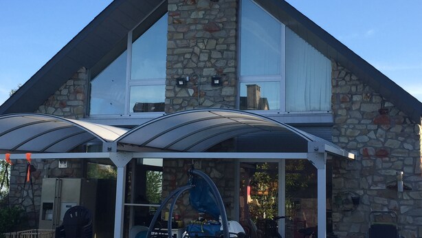 Un edificio de piedra con un invernadero de vidrio, una chimenea de piedra y un cielo azul despejado.