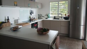 Eine moderne Küche mit einer zentralen Kochinsel, einem Einbauofen, einem Kühlschrank und einem Fenster mit Blick auf Grünflächen.