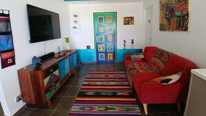 Ein Wohnzimmer mit Fernseher, farbenfroher Kunst, einem roten Sofa und einem gemusterten Teppich.