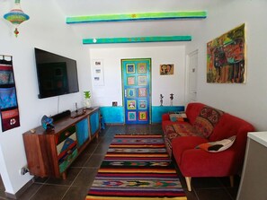 Ein Wohnzimmer mit Fernseher, farbenfroher Kunst, einem roten Sofa und einem gemusterten Teppich.