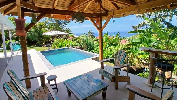 Ein überdachter Außenbereich mit Pool, Liegestühlen und Meerblick.