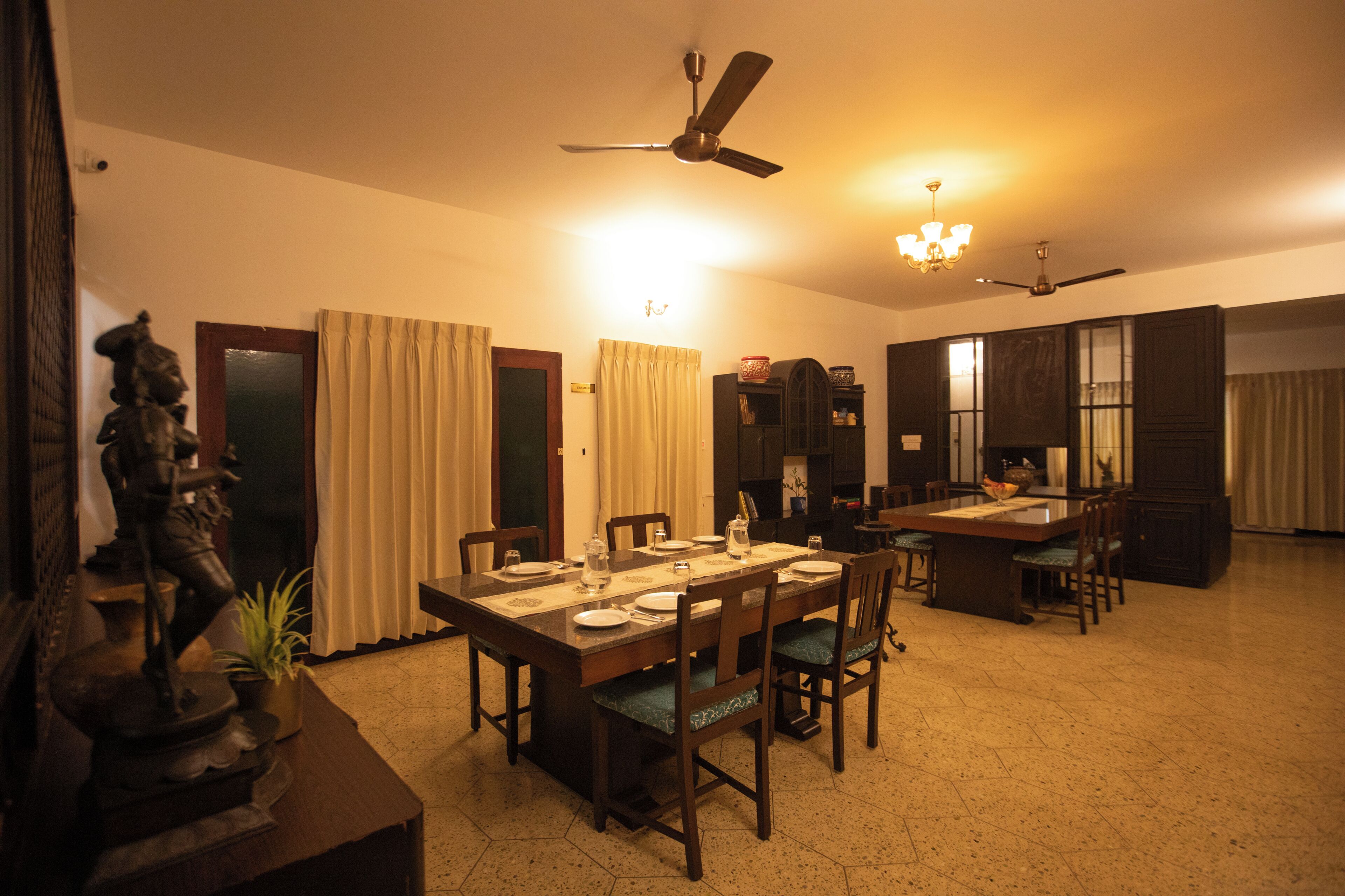 A dining area with a table set for four, chairs, a ceiling fan, and a chandelier.