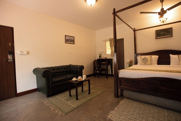 Une chambre à coucher avec un lit à baldaquin, un canapé sombre, une petite table avec une tasse et une assiette, et un bureau avec une chaise.