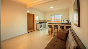 A modern kitchen with a bar area, a dining space with a sofa and chairs, and a large window providing a view.