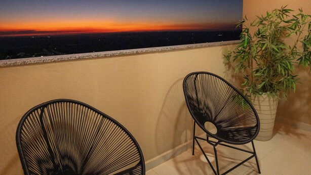 A balcony with two chairs, a potted plant, and a sunset view.