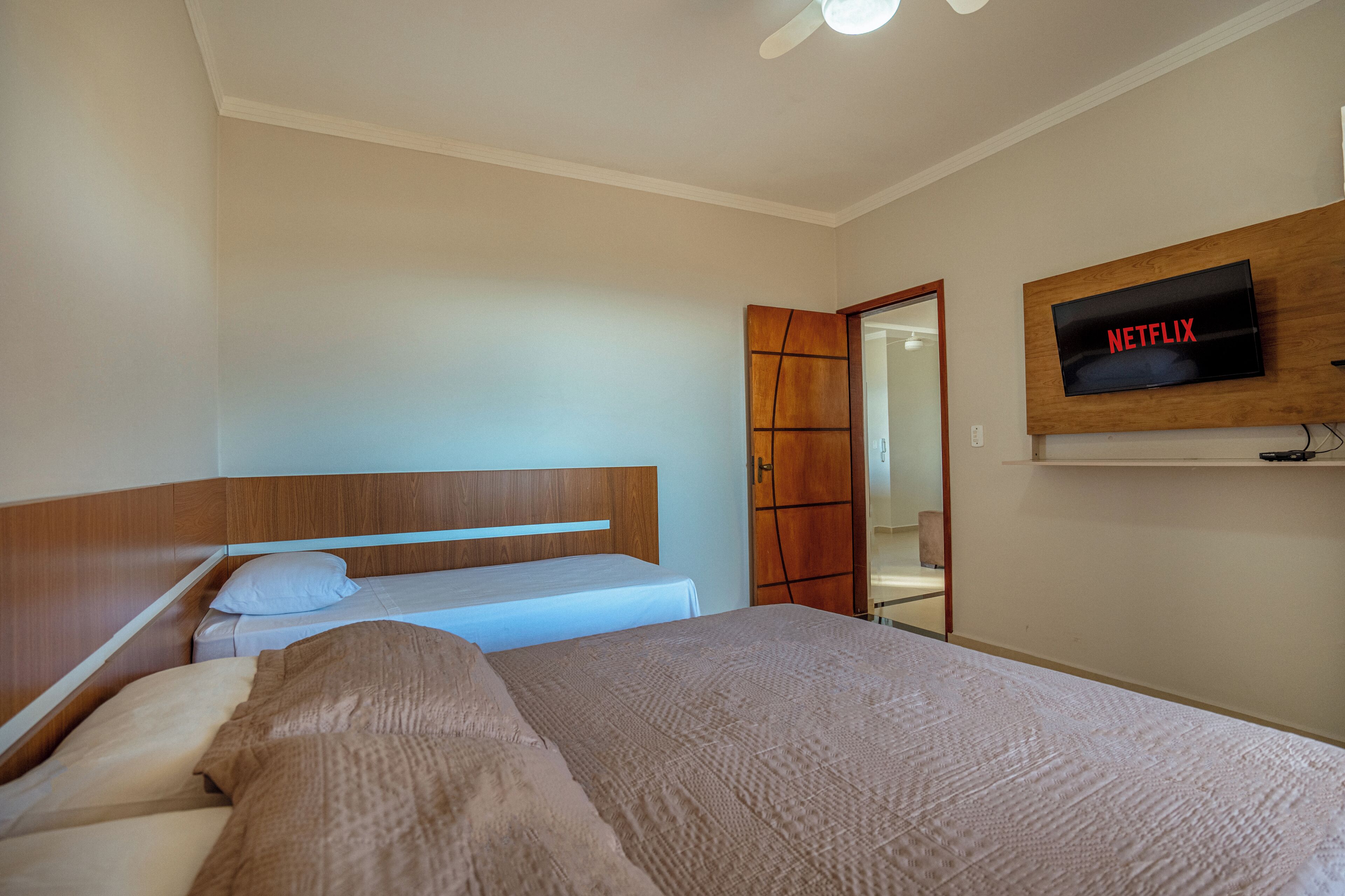 Una camera da letto con un letto, una testata in legno, una TV fissata al muro e una porta che dà su un'altra stanza.