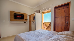 A bedroom with a bed, a TV mounted on the wall, a wooden door, and a view of the outside.