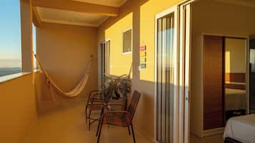 A balcony with a hammock, wicker chairs, a potted plant, and a sliding glass door leading to a bedroom.