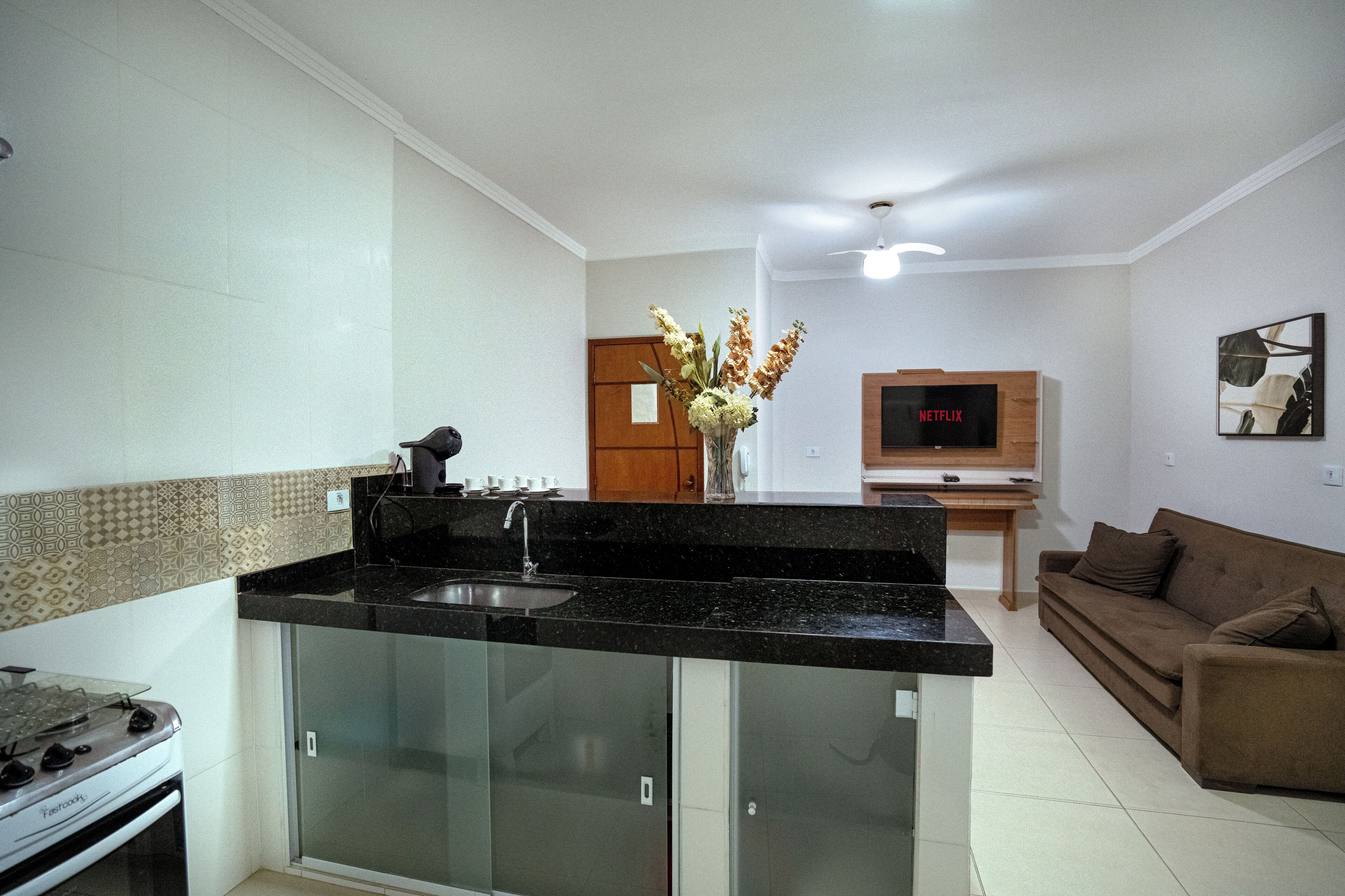 Eine moderne Küche mit Einbauherd, Spüle und einem Schrank mit Glastür. Im Wohnbereich befindet sich ein Holzkasten und ein Flachbildfernseher.