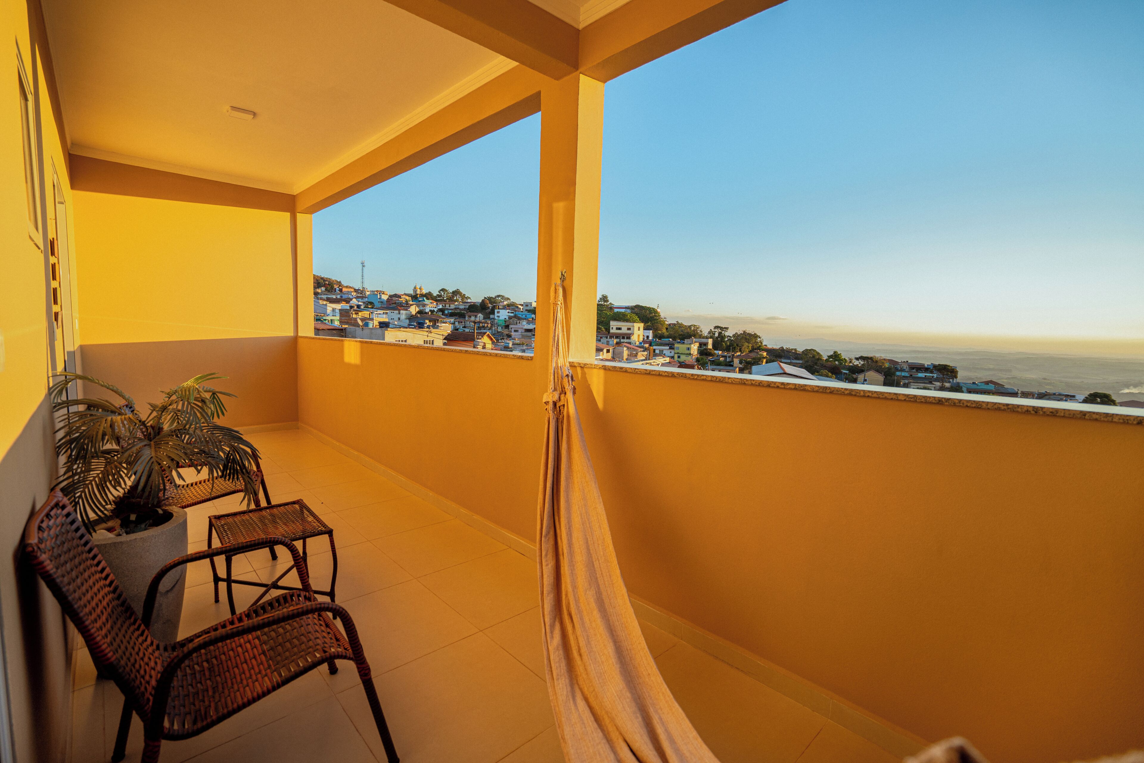 Uma varanda com vista para uma cidade costeira, móveis de vime e um vaso de planta.
