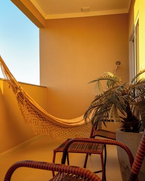 A hammock, wicker chairs, and a potted plant in a room with a plain wall and a window.