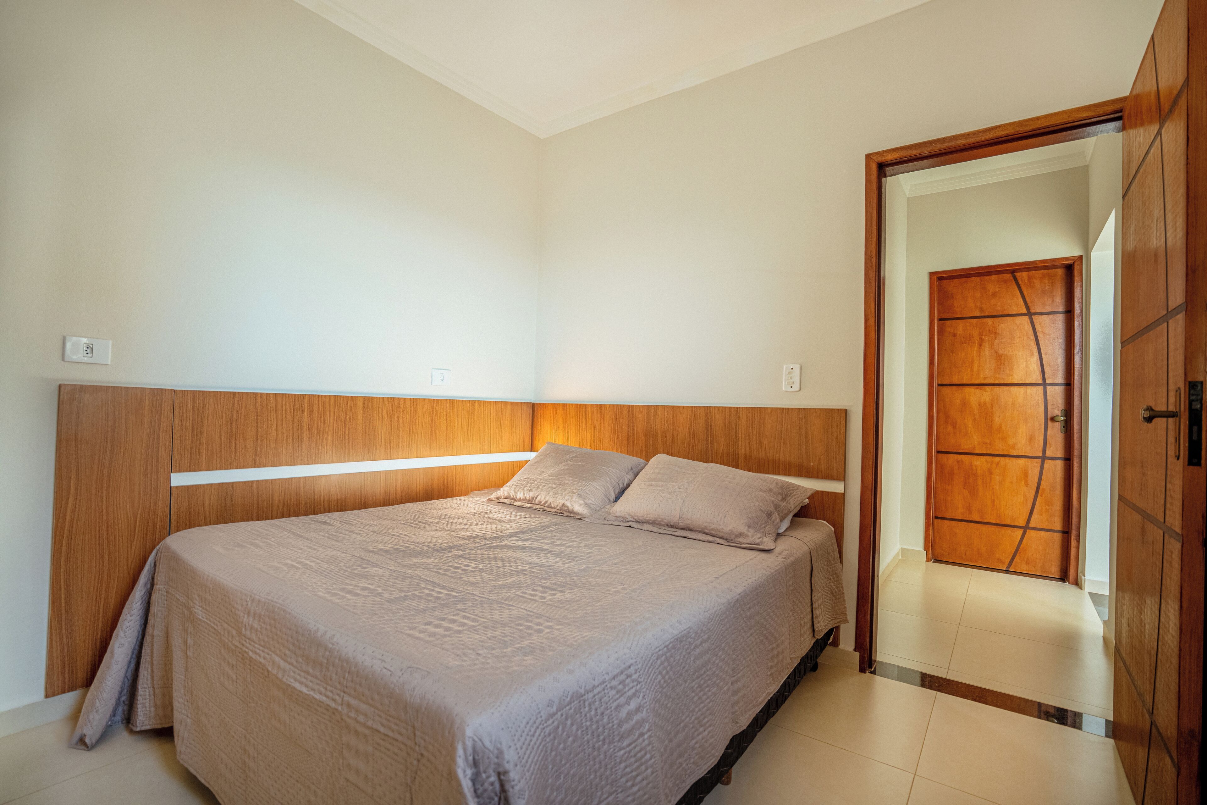 A bedroom with a bed, wooden headboard, and a door leading to another room.