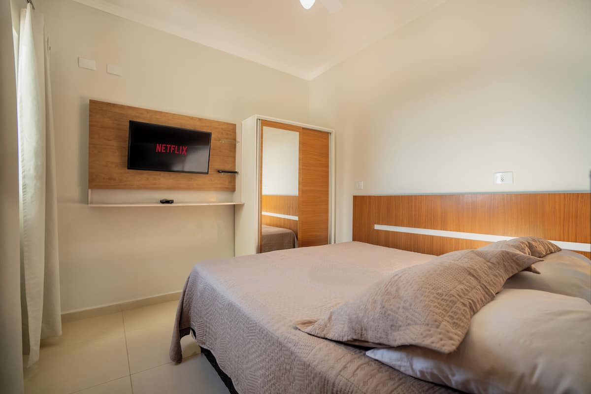 Un dormitorio con una cama, un televisor montado en un estante de madera, un espejo y una puerta.
