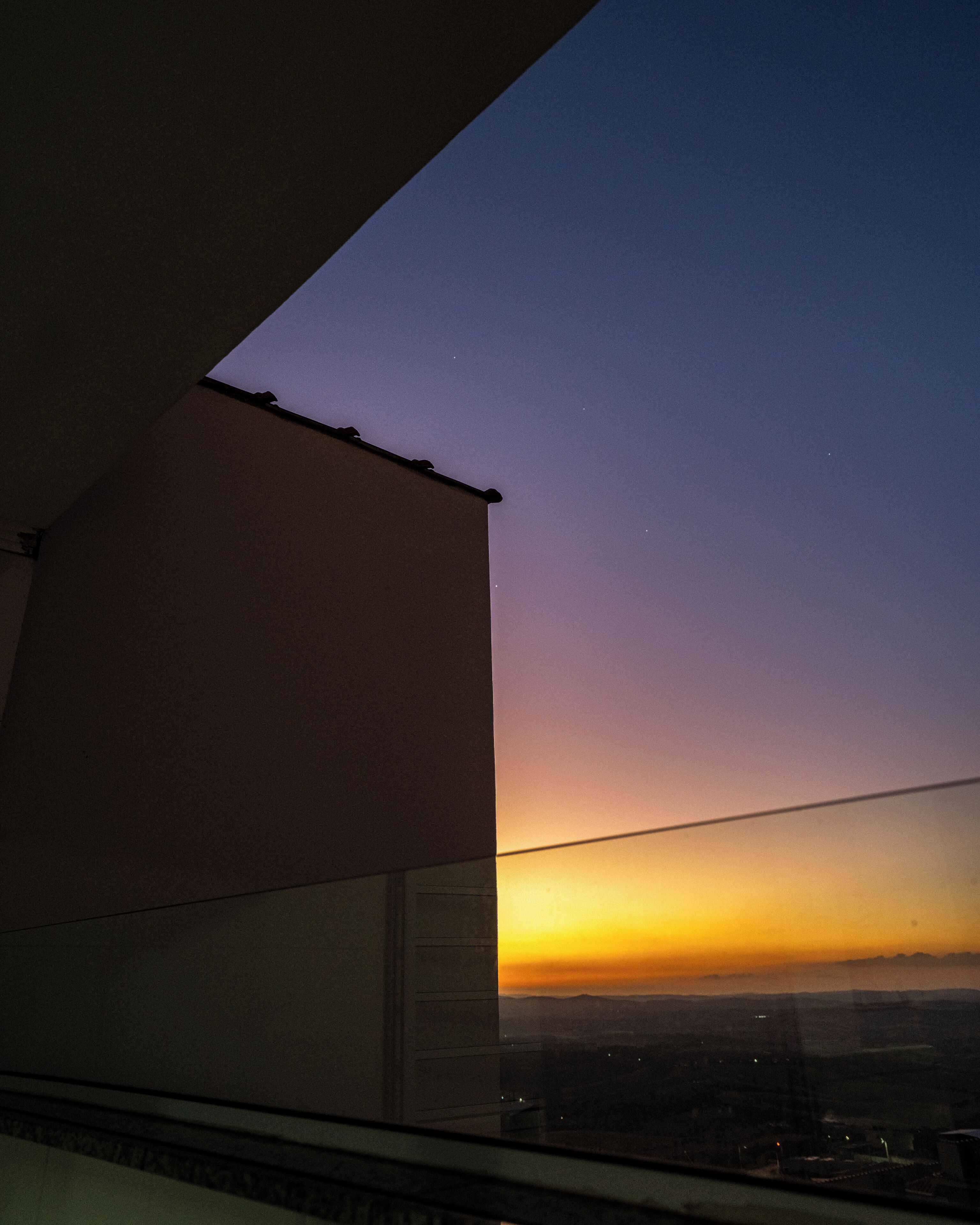 A view from a window with a building's edge and a sunset.