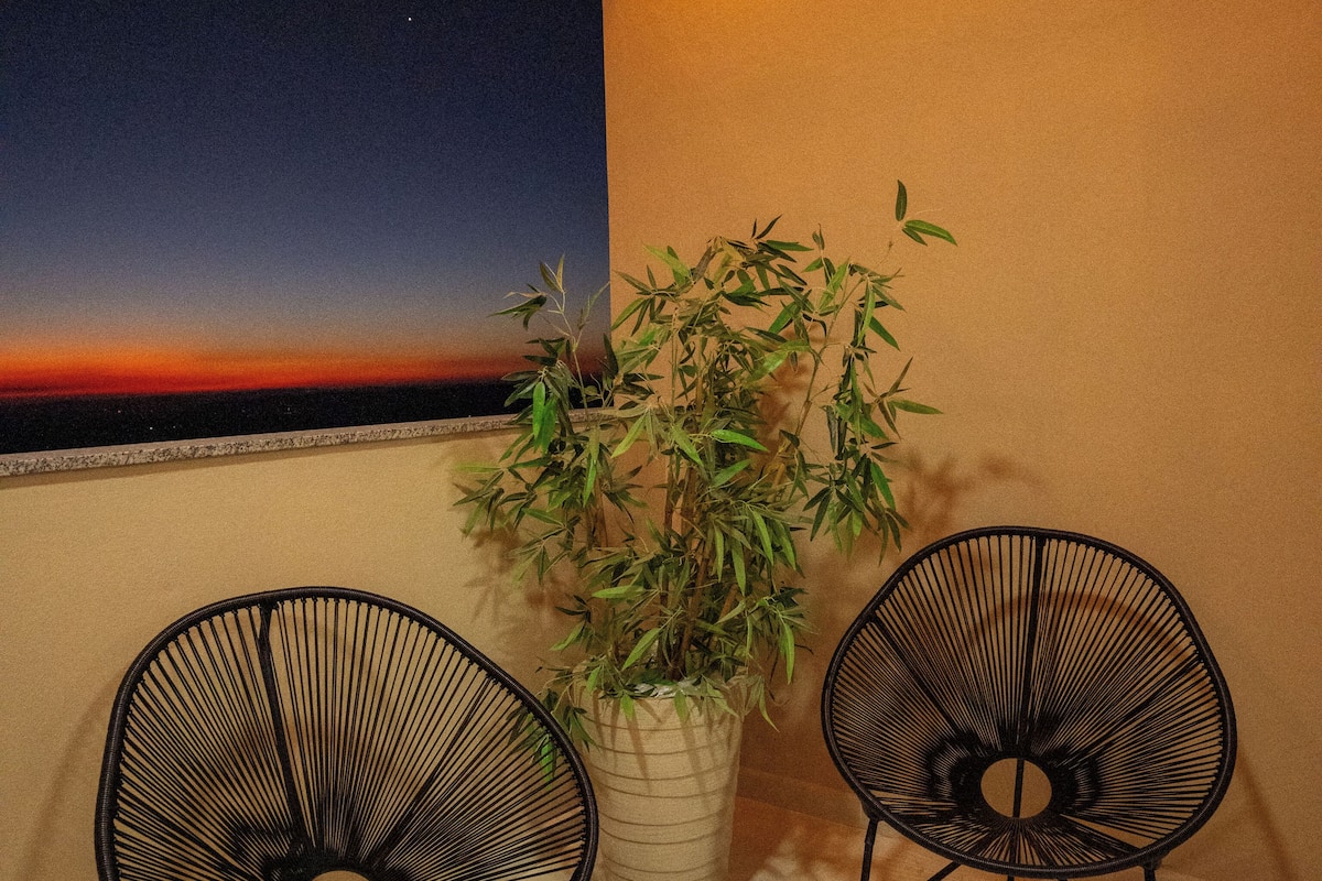 Dos sillas de diseño minimalista negras, una planta en maceta y vista al atardecer desde un balcón.