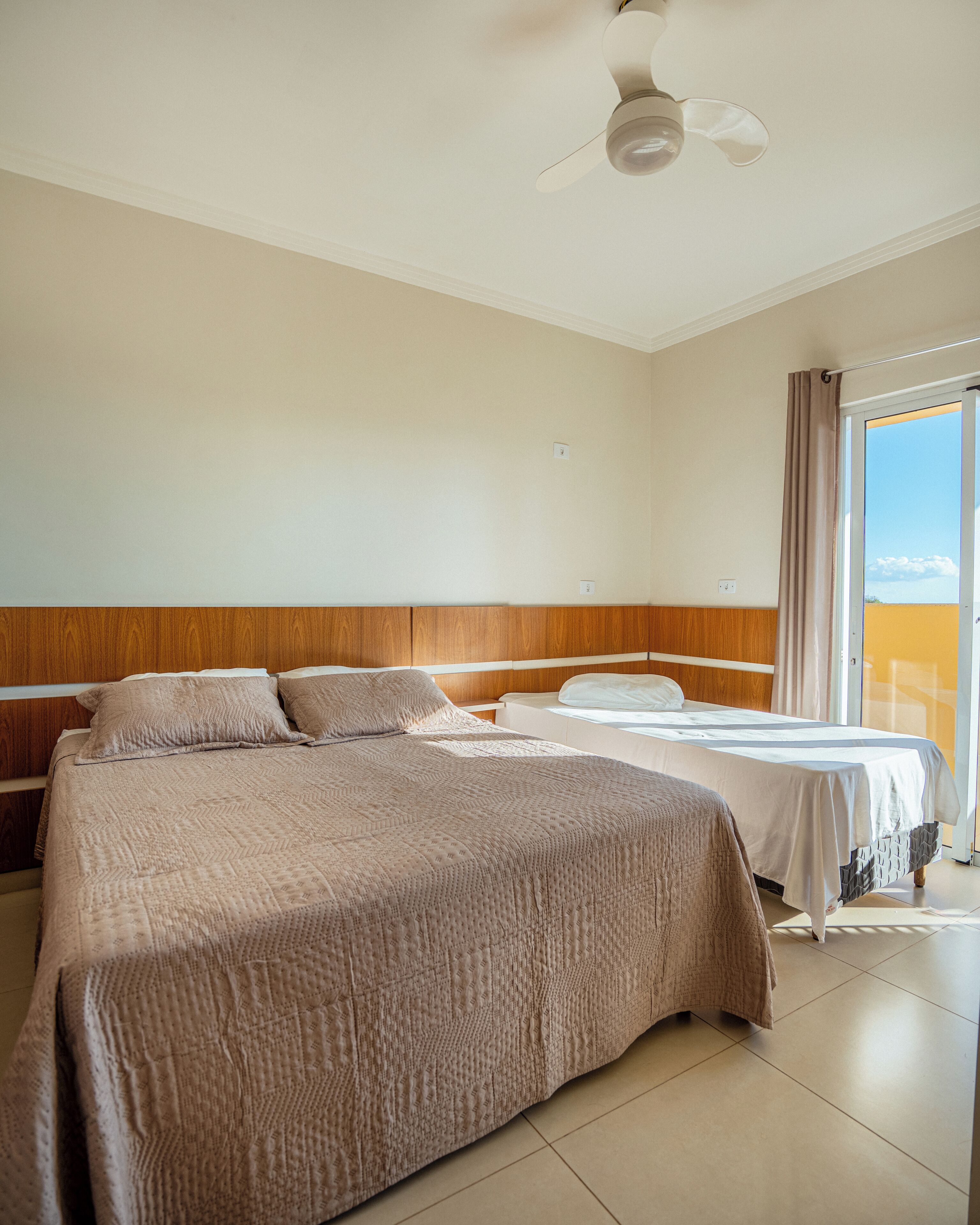A hotel room with a large bed, a smaller bed, a ceiling fan, and a sliding glass door to the outside.