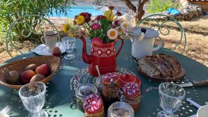 A table set outdoors with a view of a pool, featuring a vase of flowers, bread, fruit, and various jars. - Guest Room 'La Fenière' with Shared Pool, Garden & Summer Kitchen, Wi-Fi (Carcès)