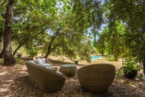 Wicker furniture under a tree, a pool in the background, and a garden setting. - Bed and Breakfast 'La Fenière' with Shared Pool, Shared Terrace and Wi-Fi (Carcès)
