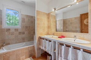 Ein Badezimmer mit zwei Waschbecken, einer Badewanne, einem Fenster mit Gitterstäben und einem Spiegel.